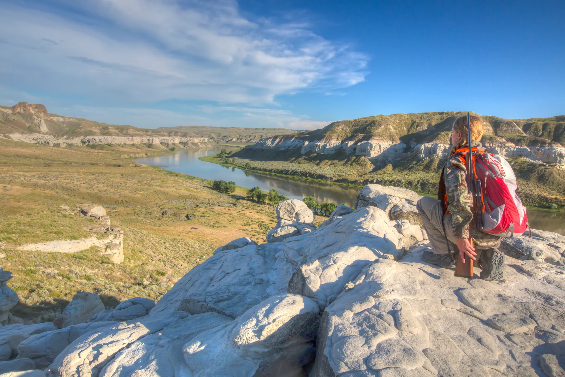 A hunter with a rifle and pack looks across the Upper Missouri River Breaks from a rocky overlook in Montana.
